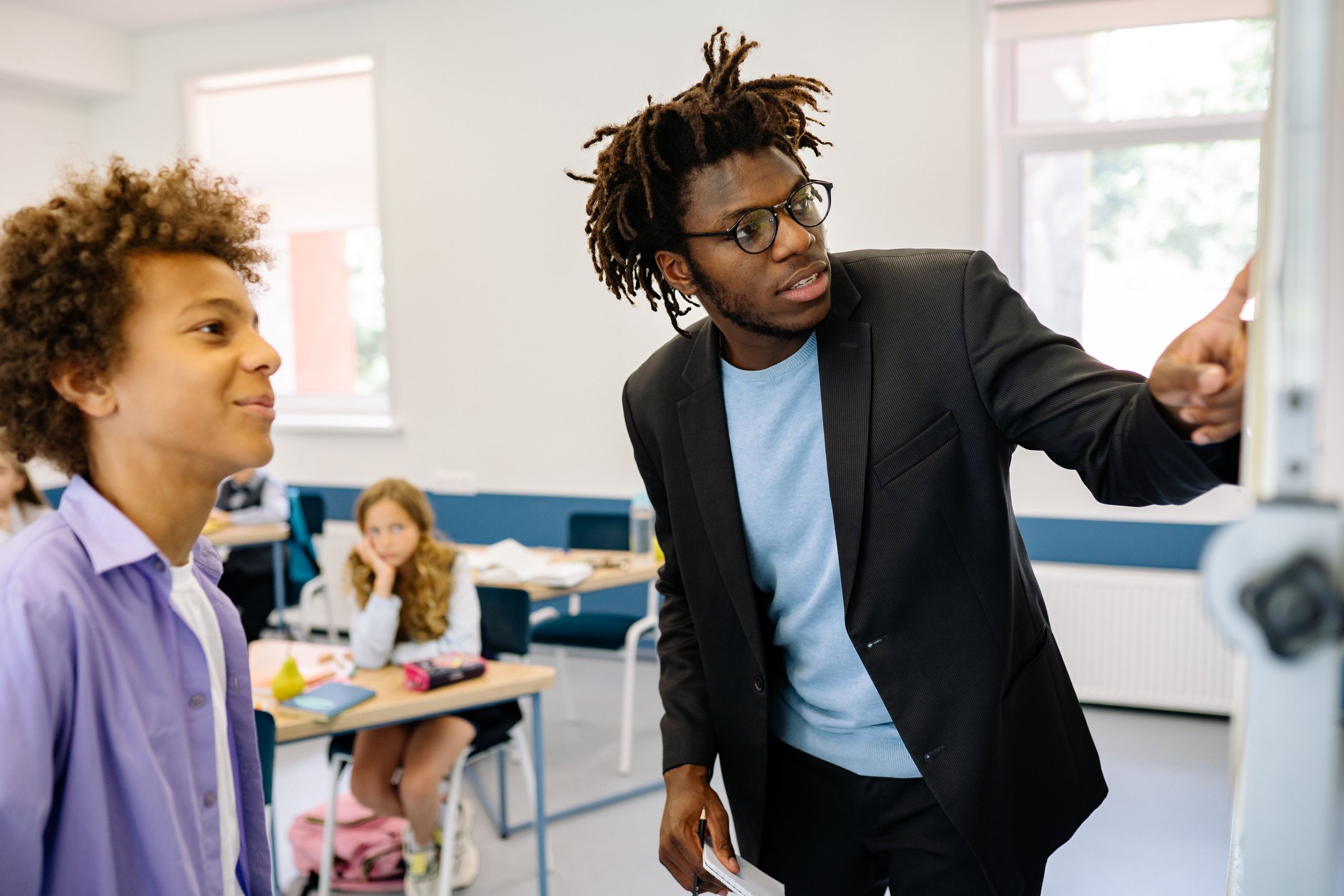 Teacher guiding a student in a classroom, promoting interactive learning.